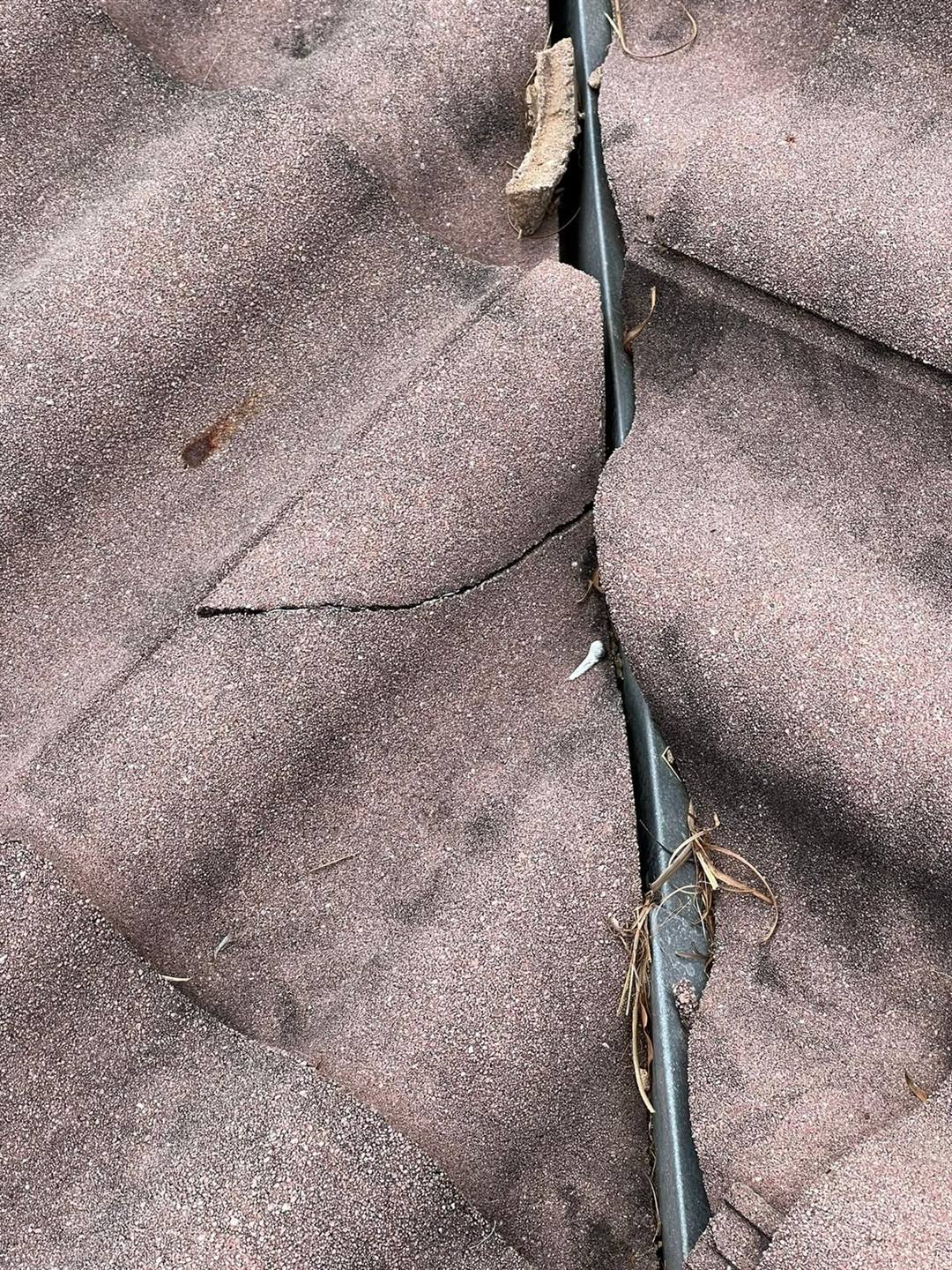 Close-up of a cracked asphalt shingle roof valley showing storm damage